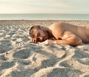 Portrait of shirtless man lying on sand at beach