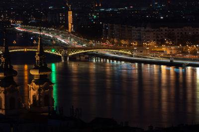 Illuminated bridge over river by buildings against sky at night