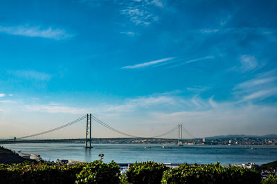 Suspension bridge over sea against cloudy sky