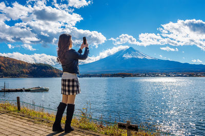 Full length of woman by lake kawaguchi photographing mt fuji