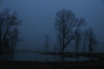 Silhouette bare trees on landscape against sky at dusk