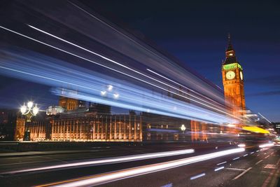 Light trails on road by big ben against sky at night