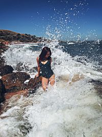 Full length of woman splashing water in sea against sky