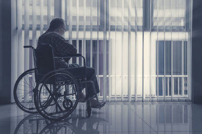 Rear view of man sitting in wheelchair by window