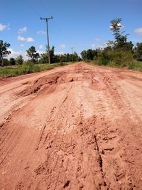 Dirt road amidst field against sky