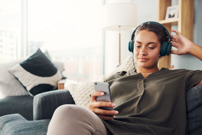 Young woman using mobile phone while sitting on sofa at home