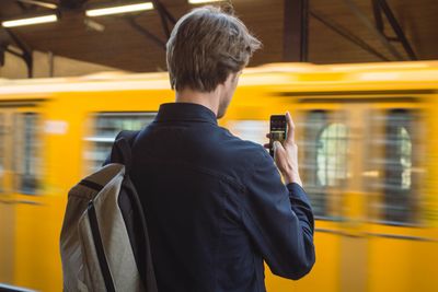 Rear view of man photographing blurred train at station