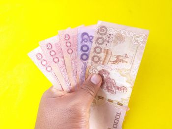 Close-up of hand holding paper against yellow background