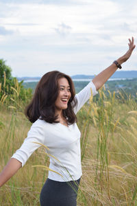 Happy young woman standing on field against sky