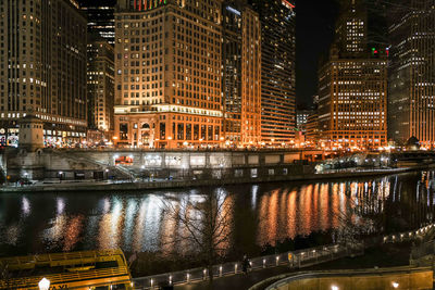 Illuminated buildings by river in city at night
