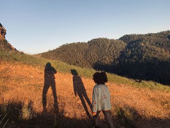 Rear view of friends standing on field against clear sky