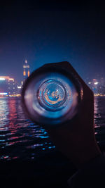 Person holding illuminated lighting equipment in sea against sky at night