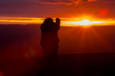 Silhouette woman standing against orange sky during sunset