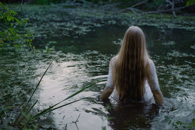 A woman in a white dress walks into a swamp.