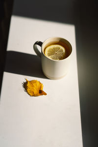 Flat lay of pumpkins, dried leaves, accessories and tea with lemon in cup on wooden background.