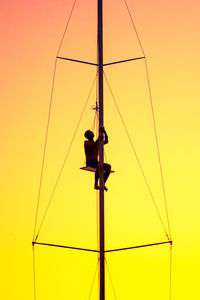 Low angle view of man sitting on mast against sky