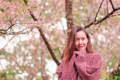 Mid adult woman wearing sweater while standing against cherry tree