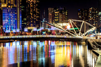 Illuminated bridge over river by buildings in city at night