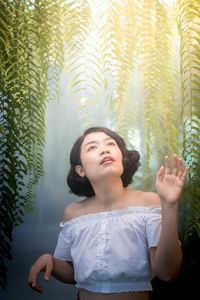 Portrait of young woman looking up against trees