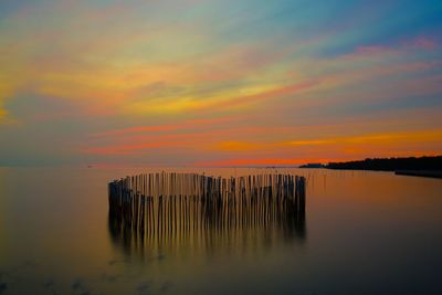 Wooden posts in sea against romantic sky at sunset