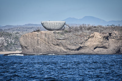 Deck chairs on rocks by sea against sky