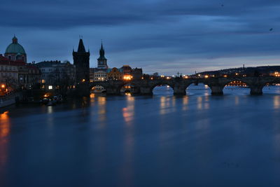 Bridge over river in city against sky at dusk