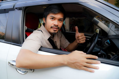 Portrait of man showing thumbs up while sitting in car