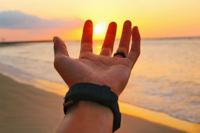 Midsection of person hand on sea during sunset