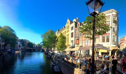 People in canal amidst buildings against clear blue sky