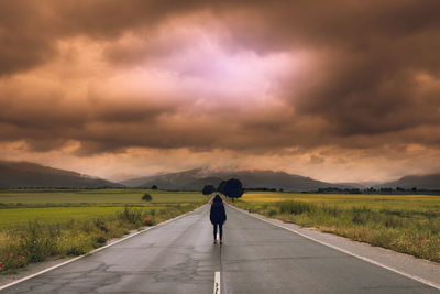 Rear view of person standing on road against cloudy sky