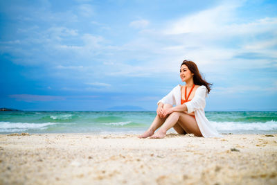 Woman sitting on beach by sea against sky