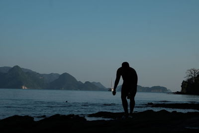 Rear view of silhouette man standing on sea against clear sky