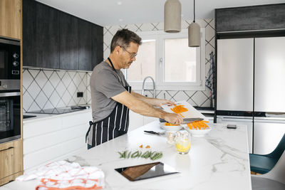 Man putting chopped carrots in bowl preparing food at home