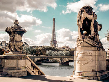 Sculptures and eiffel tower in city against cloudy sky