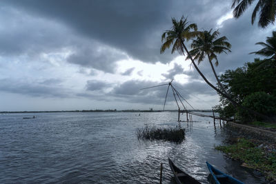 Scenic view of calm sea and palm trees against cloudy sky