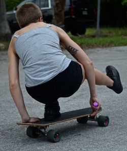 Rear view full length of woman riding longboard on road