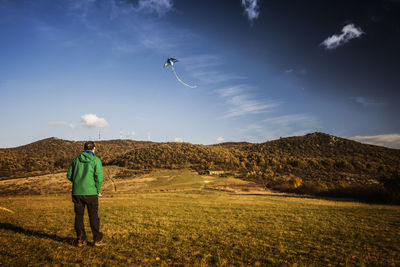 Rear view of man flying kite while standing on field against sky