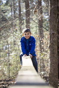 Portrait of smiling boy on wooden railing by tree at forest