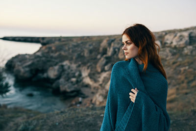 Woman standing on rock by sea against sky