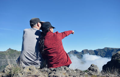Rear view of couple sitting on mountains against clear blue sky