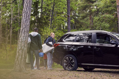 Multi-ethnic family standing with by car amidst trees