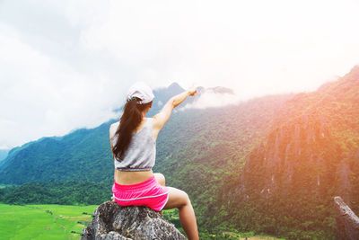 Rear view of young female hiker sitting on rock against mountain