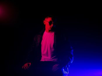 Portrait of young man standing against black background