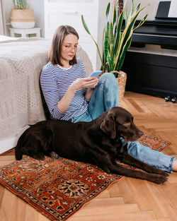 Woman using mobile phone sitting with dog at home