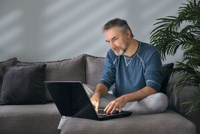 Young man using laptop while sitting on sofa at home