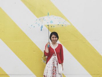Portrait of smiling mature woman holding umbrella while standing against wall