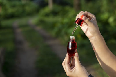 Selective focus red facial serum bottle in asian woman's hand nature background 