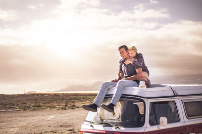 Couple embracing while sitting on vehicle