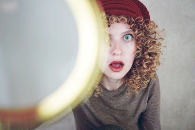 Portrait of shocked young woman behind magnifying glass against gray background
