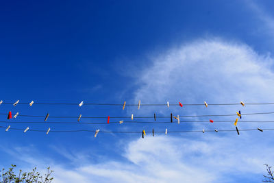 Low angle view of clothespins hanging from clotheslines against blue sky
